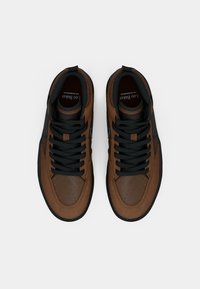 Ein Paar braune und schwarze High-Top-Sneaker mit schwarzen Schnürsenkeln, von oben auf einem einfachen weißen Hintergrund betrachtet.