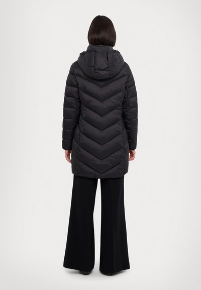 Doudoune noire avec un motif en chevrons, dotée d'une capuche et d'un design mi-long, associée à un pantalon large noir.