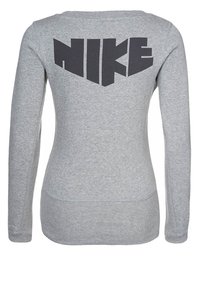 Šedá dlouhá rukávová košile vyrobená z měkkého materiálu, s velkým černým logem "NIKE" na zadní straně, s obepínajícím střihem a zakřiveným lemem.