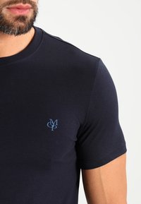 T-shirt in cotone blu navy con collo rotondo, maniche corte e un piccolo logo blu sull'area sinistra del petto. Texture liscia.