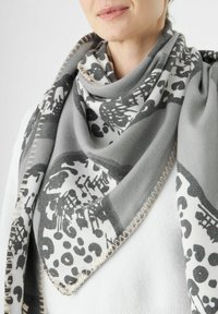Écharpe grise et blanche à motifs avec des designs abstraits, dotée d'une texture douce et de détails de couture contrastants le long des bords.