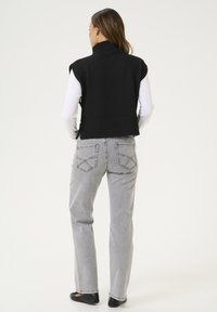 Čierny pletený bezrukávový sveter s vysokým golierom, skombinovaný so svetlošedými džínsami s dizajnom zadných vreciek a plochými čiernymi topánkami.