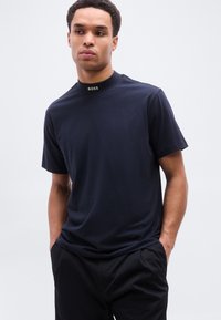 Μπλε σκούρο κοντομάνικο μπλουζάκι από βαμβάκι, με ψηλό γιακά και χρυσή λογότυπη λεπτομέρεια στο λαιμό. Ομαλή υφή.