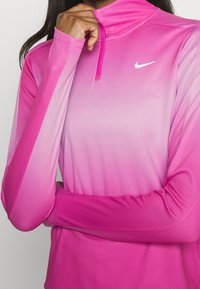 Maglietta sportiva a maniche lunghe rosa con design a gradiente, colletto con mezza zip e logo Nike sul petto. Tessuto morbido e leggero.