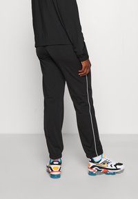 Pantaloni sportivi neri con striscia laterale bianca, vita elastica e gambe tapered, abbinati a scarpe da ginnastica sportive multicolori.