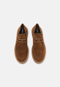 Chaussures décontractées à lacets en daim marron avec semelles épaisses cousues, vues de dessus sur un fond blanc uni.