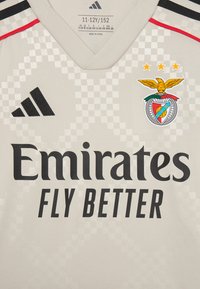 Sivi nogometni dres s V-izrezom, koji ima karirani uzorak, crni Adidas logo, veliki tekst "Emirates Fly Better" i simbol Benfice s tri zvjezdice.