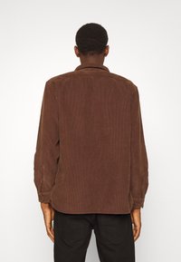 Braunes Cord-Hemd mit Button-Down-Kragen, langen Ärmeln und geradem Saum. Strukturierter Stoff mit vertikalen Rippen.