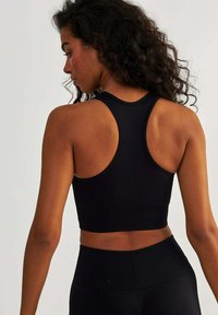 Crop top de sport noir avec un dos nageur, présentant des rayures horizontales texturées et une coupe ajustée. Tissu doux, détails de couture minimaux.