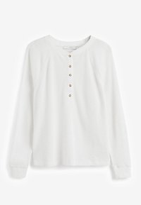 Chemise henley blanche à manches longues avec un col rond et cinq boutons dorés sur le devant.