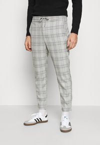 Grijze geruite broek met een elastische tailleband en trekkoord, met een aansluitende pasvorm. Draag het met witte sportschoenen met zwarte accenten.
