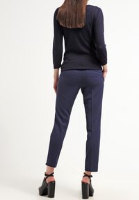 Marinblå skräddarsydda byxor i ett slätt tyg med en elegant design. Modellen bär svarta klackskor med ankelsnoddar.