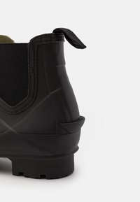 Botte en caoutchouc noir avec des côtés texturés, une cheville flexible et une languette arrière pour un enfilage facile. Présente une semelle robuste et striée pour une bonne adhérence.