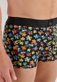 Men's black boxer shorts featuring a playful puzzle piece pattern in bright colors. The waistband is solid black with branding detail.