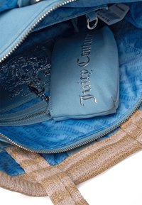 Niebieska torba na zamek błyskawiczny w środku z jaśniejszym niebieskim woreczkiem, z logo "Juicy Couture" w metalicznym srebrze. Wyłożona wzorzystą tkaniną.