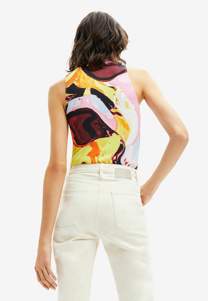 Kleurrijke, gemusterde mouwloze top met abstracte swirls in roze, geel en zwart, gecombineerd met witte high-waisted broeken.