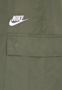 Olivgrön cargoshorts med en frampocket, prydda med en vit broderad Nike-logotyp. Tillverkade av ett slitstarkt tyg med synliga sömdetaljer.