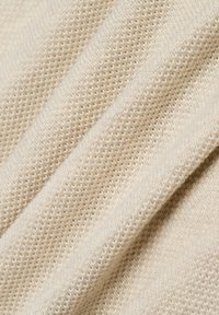 Beiger Strickstoff mit einem strukturierten, offenen Webmuster, das eine weiche Oberfläche und einen sanften Fall in gefalteten Lagen zeigt.