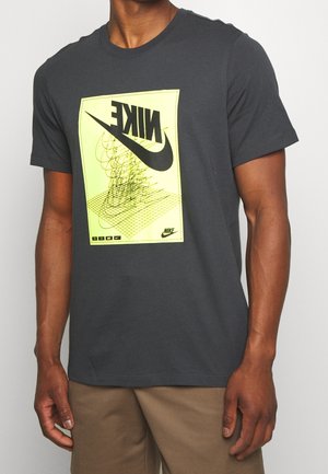 Camiseta de algodón gris con un gran logo de Nike amarillo y un diseño gráfico en el frente, con mangas cortas y cuello redondo.