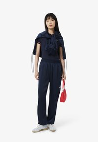 Navy athletic set with a cropped top and loose pants, featuring elastic waistband, paired with a red handbag and white sneakers.