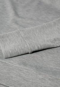 Felpa grigia con una texture liscia, dotata di polsini a costine e un logo ricamato nella parte inferiore, che mette in risalto un design rilassato.