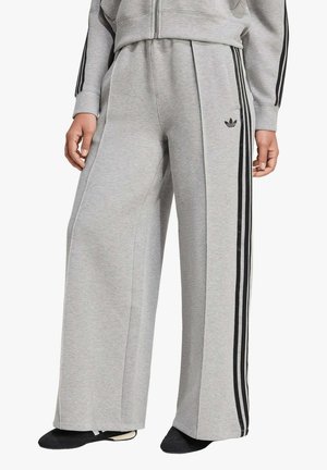Pantaloni della tuta grigi a gamba larga con strisce nere sui lati, caratterizzati da una vestibilità comoda e una leggera lucentezza. Accento con logo sull'anca sinistra.