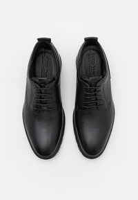 Chaussures en cuir noir à finition lisse, design à lacets, bout arrondi et accents texturés sur la tige. Semelle en caoutchouc profilée basse.