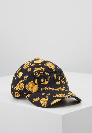 Czarna czapka bejsbolowa z ozdobnym złotym wzorem barokowym i wyhaftowanym napisem "Versace Jeans Couture" z przodu, prezentowana na białej powierzchni.