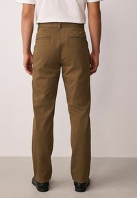 Khaki värvi püksid sirge lõikega, millel on kaks tagataskut, vööaugud ja sile tekstuur. Sobitatud lihtsa valge t-särgiga.