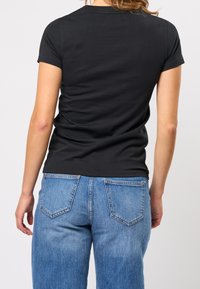 Černé tričko s krátkým rukávem, přiléhavý střih, vyrobené z měkké bavlny. Kombinováno se světle modrými džíny s vysokým pasem a zadními kapsami.