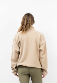 Beiger Fleece-Pullover mit hohem Kragen, lockerer Passform und gerippten Bündchen. Der Stoff hat eine weiche Textur und keine sichtbaren Muster oder Akzente.