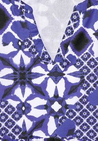 Blå och vit mönstrad tyg med geometriska mönster, som har en djup V-ringning och en slät, texturerad yta.