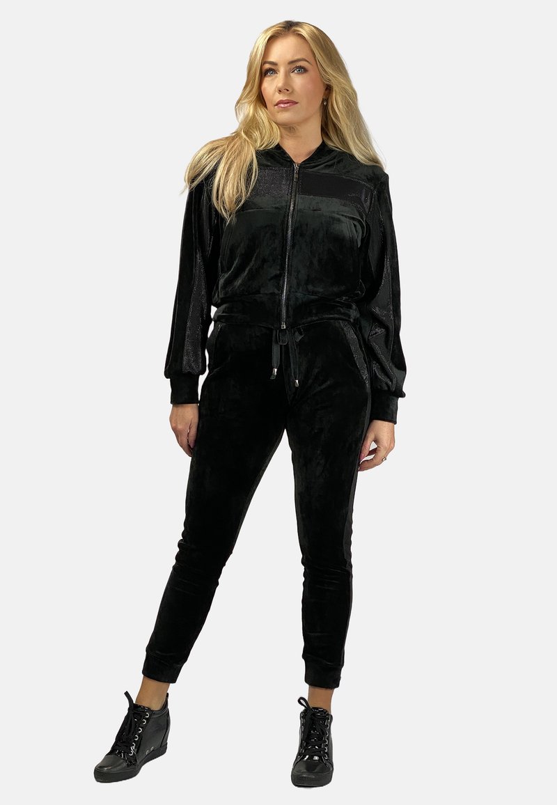 Czarny welurowy dres składający się z kurtki na zamek błyskawiczny z bocznymi kieszeniami oraz dopasowanych spodni. Uzupełniony czarnymi sznurowanymi butami.