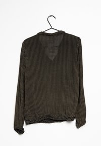 Blouse noire à manches longues avec un petit motif de points dorés, coupe ample, encolure légèrement froncée et ourlet arrondi. Suspendue sur un cintre noir.