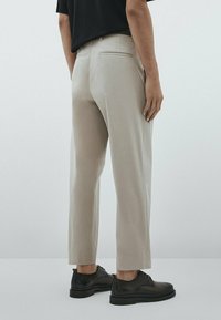 Beige skräddarsydda byxor med rak passform, med en bakficka, som bärs med svarta dressade skor. Slätt tyg och ren design.