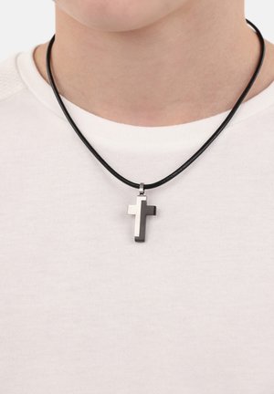 Kreuzanhänger-Halskette mit einem Schwarz- und Silberschema, hängt an einem schwarzen Lederband und wird über einem weißen Hemd getragen.