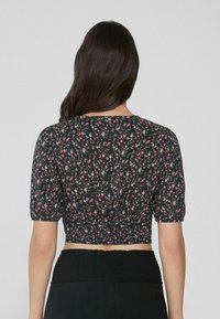 Schwarzes Blumen-Crop-Top mit kurzen Puffärmeln, das einen gerafften Saum und kleine rosa-weiße Blumenmuster aufweist.