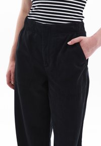 Zwarte, relaxte broek van katoen met zijzakken en een gladde textuur. Hoge tailleband met subtiele stikdetails.