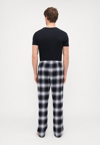 T-shirt noir à manches courtes pour homme associé à un pantalon de pyjama à carreaux gris et noir, avec une coupe décontractée et une taille élastique.