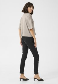 T-shirt beige court à manches courtes, associé à un jean slim noir et des mules noires à talons. Design simple, texture lisse.