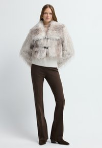 Chaqueta corta texturizada con un acabado parecido al pelo, en color marrón claro y crema, con un dobladillo blanco acanalado y cierre de toggle negro. Combina con pantalones marrones.