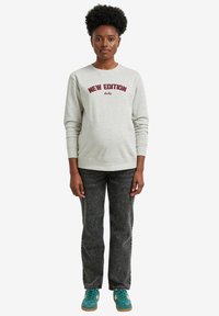 Helles graues Sweatshirt mit rotem Text "NEW EDITION baby", kombiniert mit ausgewaschenen schwarzen Jeans und türkisfarbenen Sneakern. Einfaches, lässiges Design.