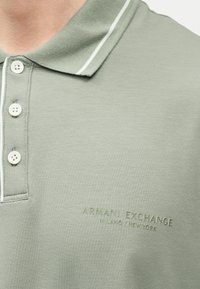 Polo vert clair avec des boutons blancs et un logo discret "Armani Exchange Milano/New York" sur la poitrine.