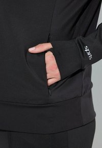 Felpa sportiva nera con tasca con zip, aperture per il pollice nei polsini e una finitura liscia e strutturata. Logo sulla manica.