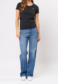 Černé tričko s krátkým rukávem a malým logem na hrudi, kombinované s světle modrými, vysokým pasem a širokými nohavicemi džíny a bílými teniskami.