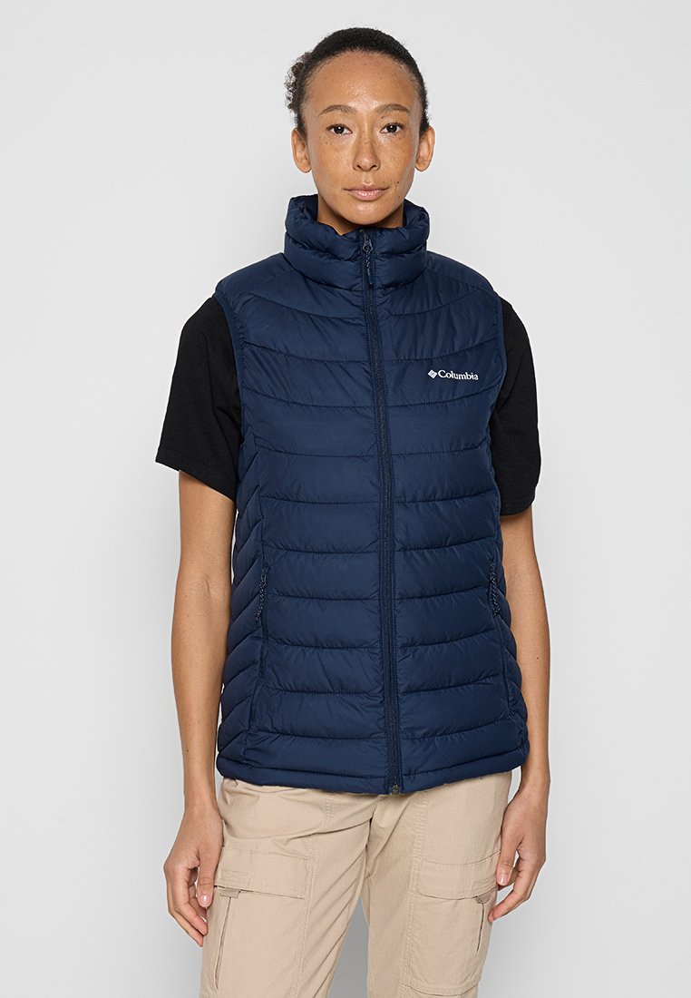 Gilet isolant bleu marine avec un col montant, design matelassé, fermeture éclair à l'avant et poches latérales, porté sur un t-shirt noir.