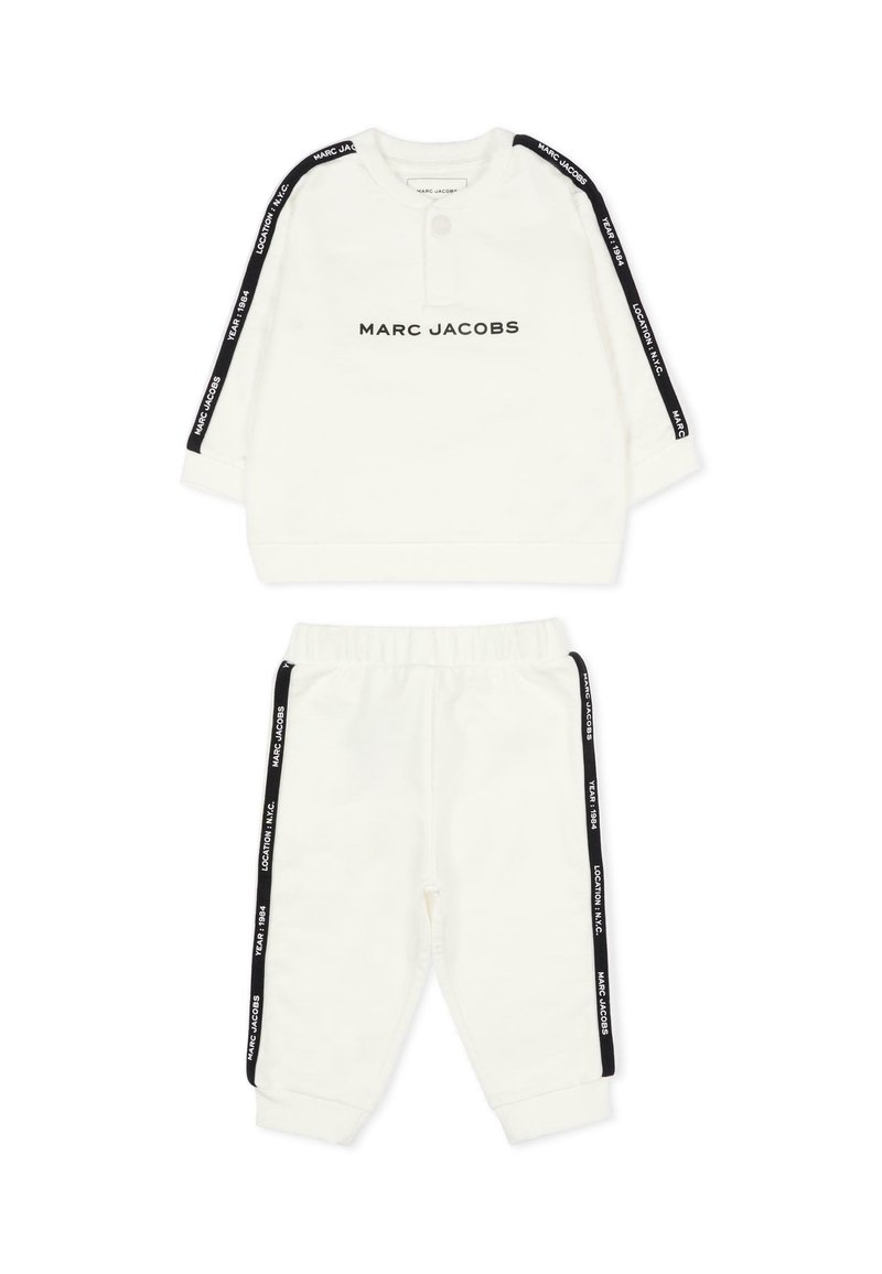 Witte twee-delige outfit gemaakt van zachte stof; voorzien van zwart logo op de voorkant, zwarte zijstrepen op de mouwen en broek, en een elastische tailleband.