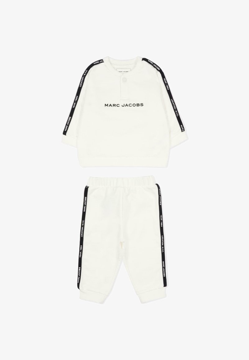 Witte twee-delige outfit gemaakt van zachte stof; voorzien van zwart logo op de voorkant, zwarte zijstrepen op de mouwen en broek, en een elastische tailleband.