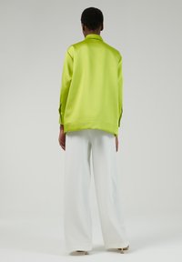 Camisa de satén verde lima con un corte relajado, mangas largas y puños, combinada con pantalones anchos blancos, que muestran una textura suave.
