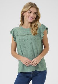 Top verde a maniche corte con maniche arricciate, in tessuto ad occhio di pernice, con delicati motivi ricamati e una vestibilità comoda.